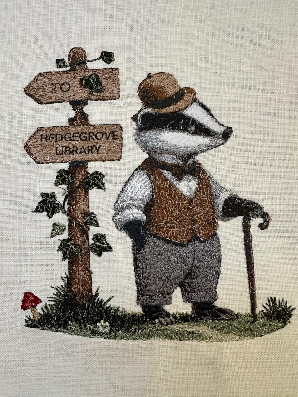 Embroidered badger at a wooden gate with signs on a textured fabric background